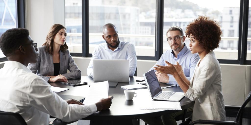 Group of people around a table, listening to one person speak